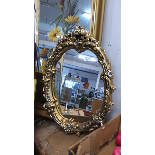 83 - Gold-colored oval mirror with floral and scroll detailing on the frame, reflecting Baroque design in... 