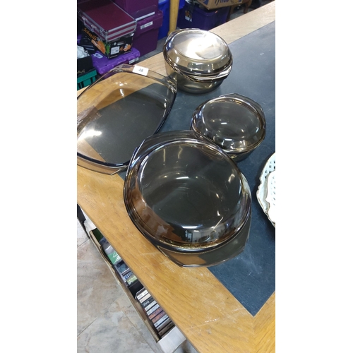 48 - Set of four smoky glass pyrex dishes with lids, varying sizes.