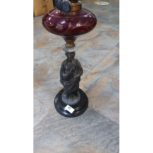 65 - Antique oil lamp with intricately detailed red glass reservoir and bronze statue base, accented with... 