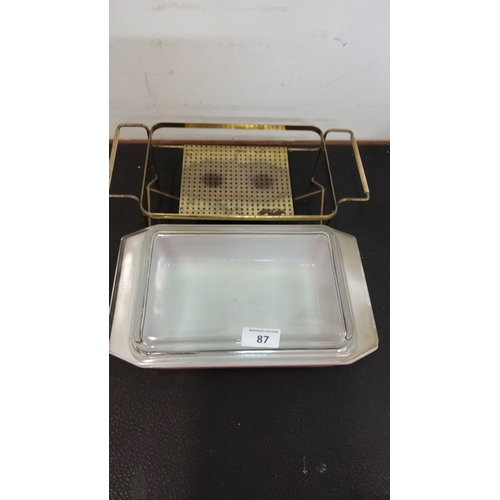 87 - Glass casserole dish features a floral design on a pink base and comes with a brass serving rack.