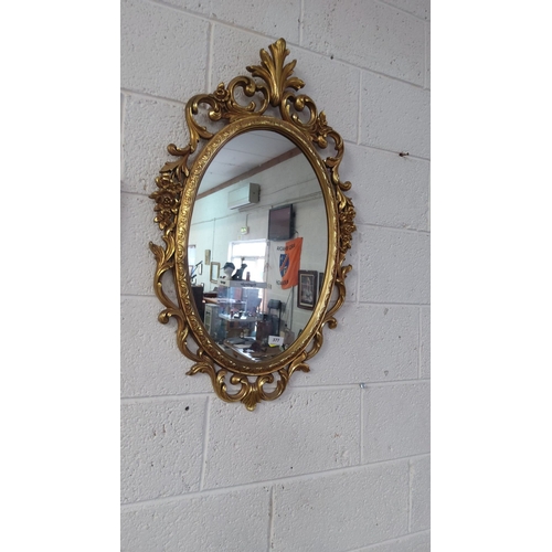 377 - Oval gilded mirror with intricately carved floral frame, approximately 80 cm x 50 cm, reflecting Roc... 