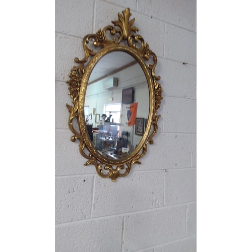 377 - Oval gilded mirror with intricately carved floral frame, approximately 80 cm x 50 cm, reflecting Roc... 