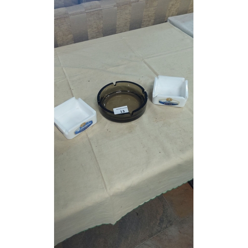 13 - Set of three ashtrays, including two white Rothmans branded pieces and one dark glass ashtray.