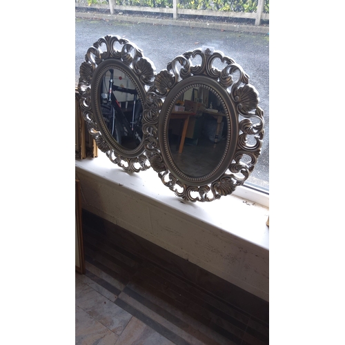 327 - Pair of oval wall mirrors with intricate silver-toned decorative frames, featuring a classic Baroque... 