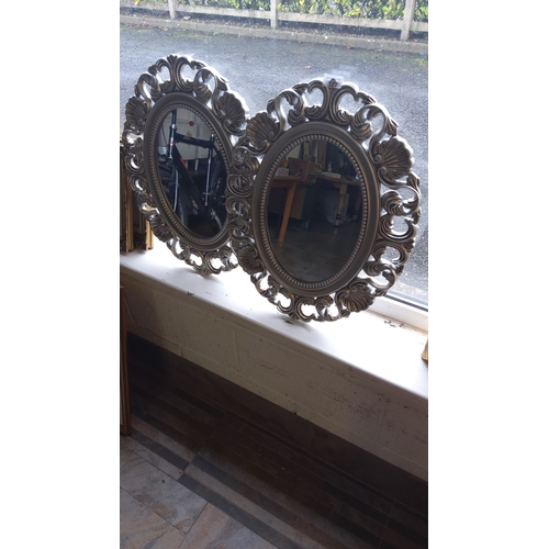 327 - Pair of oval wall mirrors with intricate silver-toned decorative frames, featuring a classic Baroque... 