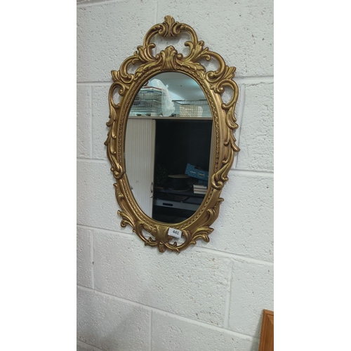 441 - Ornate oval mirror with a gold-toned frame, featuring intricate scrollwork and floral motifs. Victor... 