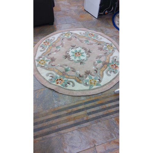 303 - Round wool rug with a floral pattern, featuring muted tones of beige, green, and red. Diameter appro... 