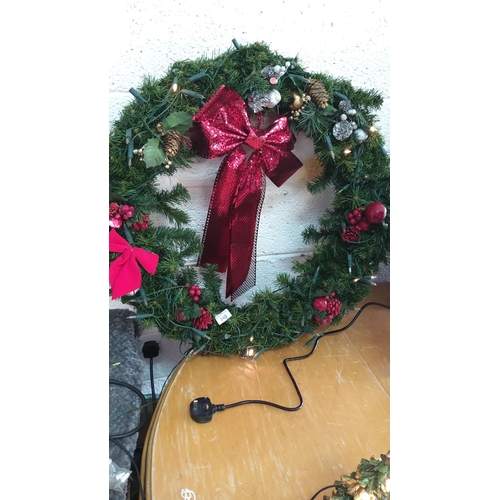 348 - Illuminated Christmas wreath with pinecones, faux berries, and a large red sequin bow. Electric powe... 