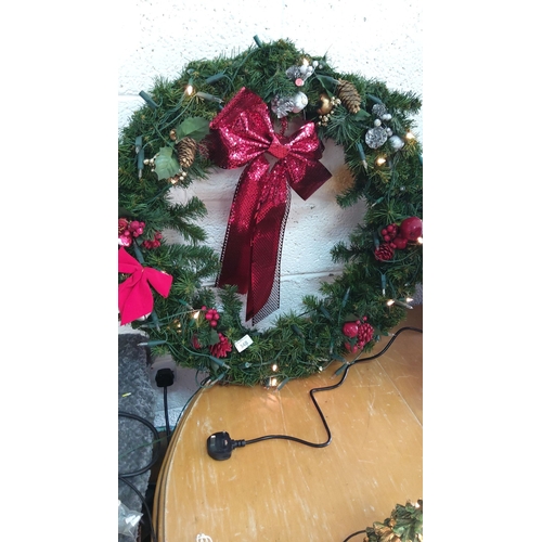 348 - Illuminated Christmas wreath with pinecones, faux berries, and a large red sequin bow. Electric powe... 