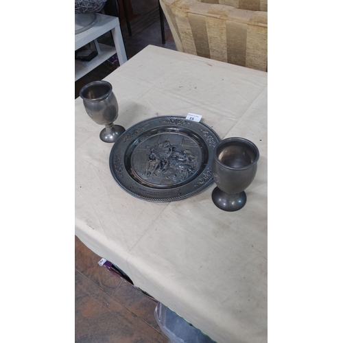 15 - Antique pewter set featuring a decorative plate with embossed figures and two matching goblets from ... 