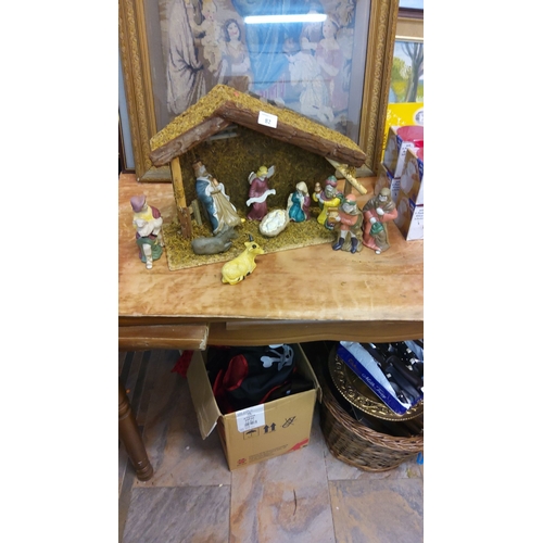 82 - Nativity scene with hand-painted ceramic figurines, housed in a rustic wooden stable.