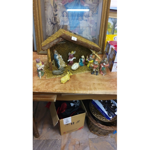 82 - Nativity scene with hand-painted ceramic figurines, housed in a rustic wooden stable.