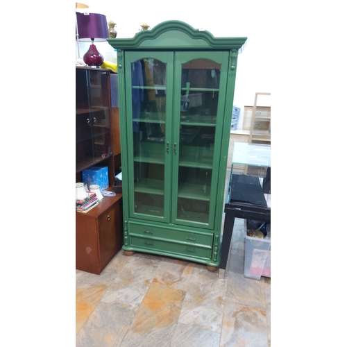 448 - Green painted wooden display cabinet with glass doors and lower drawers, featuring a curved top and ... 