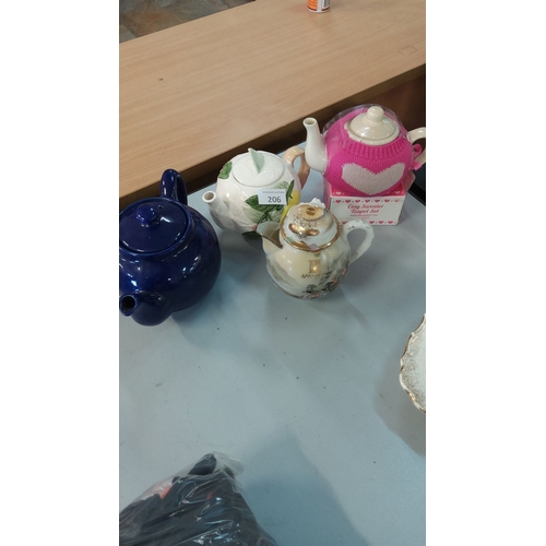 206 - Assorted Teapot Collection featuring a cobalt blue teapot, floral ceramic designs, and a pink cozy s... 