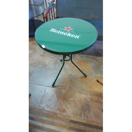 303 - Heineken-branded round café table, metal frame painted green, sturdy tripod base, and glass top feat... 