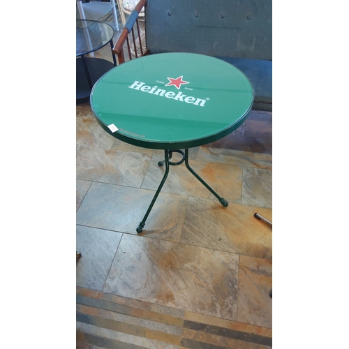 303 - Heineken-branded round café table, metal frame painted green, sturdy tripod base, and glass top feat... 