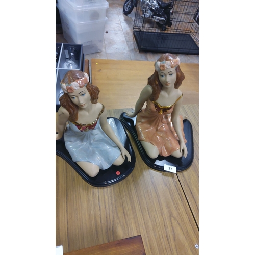 37 - Pair of hand-painted ceramic figurines, seated on black bases. Delicately detailed with floral crown... 