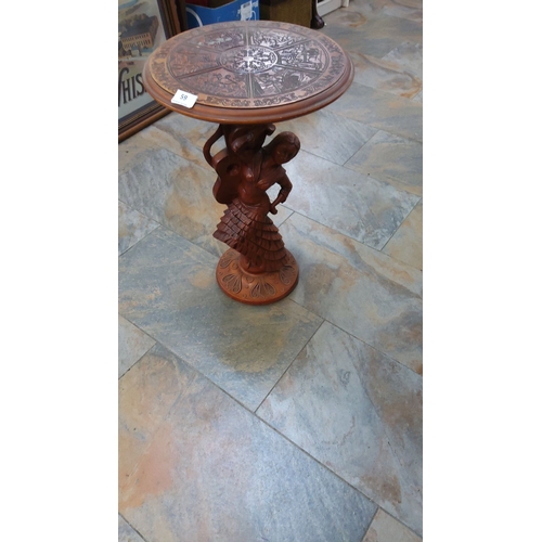 59 - Wooden side table features an intricate folkloric figure base and a detailed etched circular top.