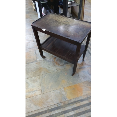 65 - Vintage wooden tea trolley with two tiers, raised edges, and caster wheels.