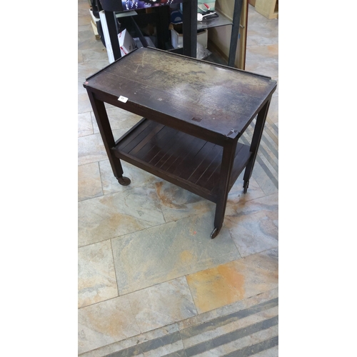 65 - Vintage wooden tea trolley with two tiers, raised edges, and caster wheels.