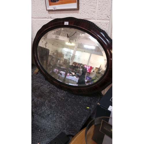 344 - Early 20th-century oval wall mirror with a mahogany veneer frame. It features a scalloped edge and a... 