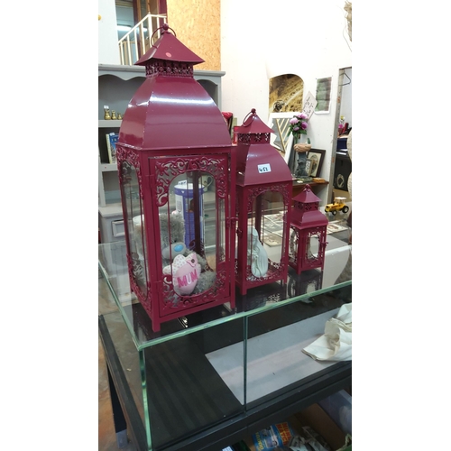 452 - Set of three burgundy metal lanterns with ornate scrollwork and glass panels. They come in graduated... 