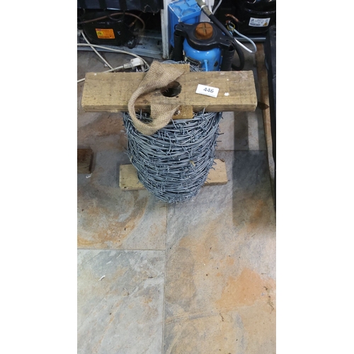 446 - Large spool of barbed wire with wooden supports.