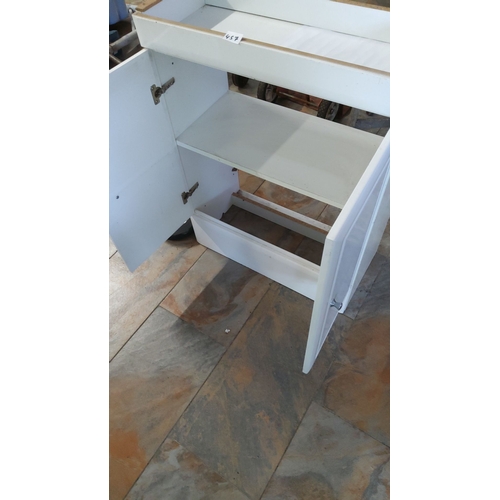 457 - White wooden cabinet with double doors, storage shelves, and a pull-out drawer. Features metal handl... 