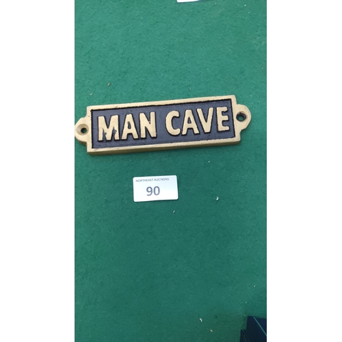 90 - Small rectangular metal wall plaque with raised gilt lettering reading “MAN CAVE” on a black recesse... 