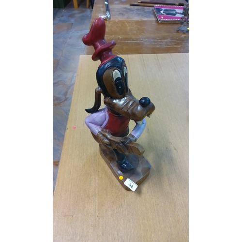 32 - Carved and polychrome-painted wooden figure of Disney’s Goofy holding a guitar, wearing tall red hat... 