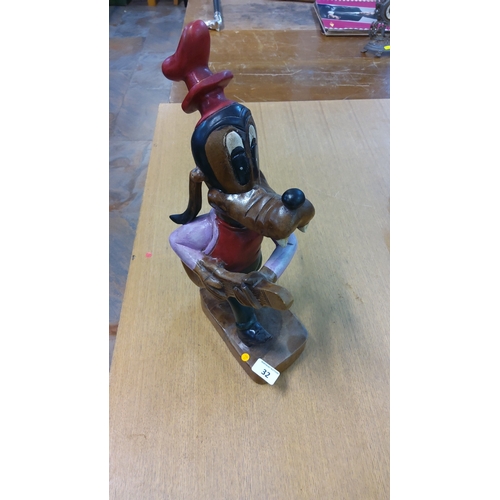 32 - Carved and polychrome-painted wooden figure of Disney’s Goofy holding a guitar, wearing tall red hat... 