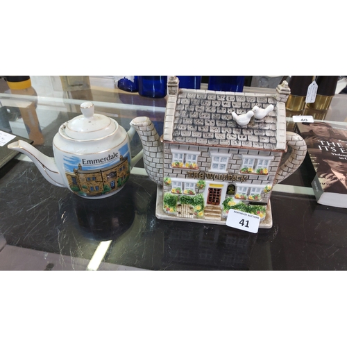 41 - Pair of Emmerdale television-themed ceramic teapots, comprising a cylindrical pot with printed homes... 