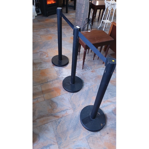 280 - Set of three black metal queue stanchions with retractable fabric belts.