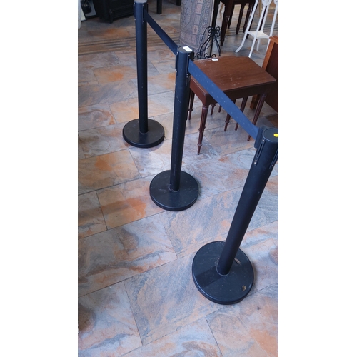 280 - Set of three black metal queue stanchions with retractable fabric belts.