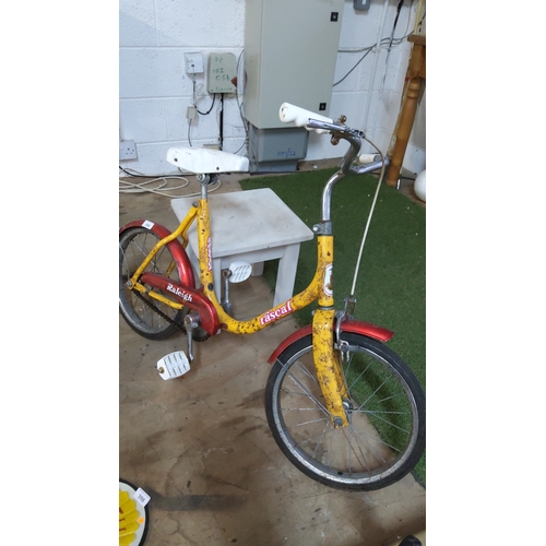 396 - Yellow and red Raleigh “Rascal” children’s single-speed bicycle with small wheels, white saddle and ... 