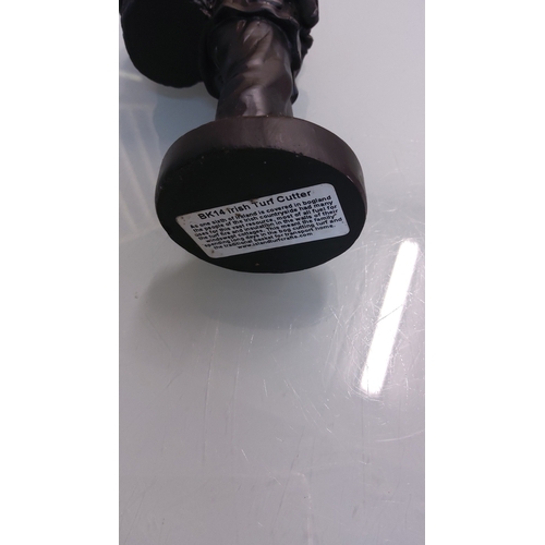 59 - A cast resin figure modelled as an Irish turf cutter carrying a creel of turf on his back, on a circ... 