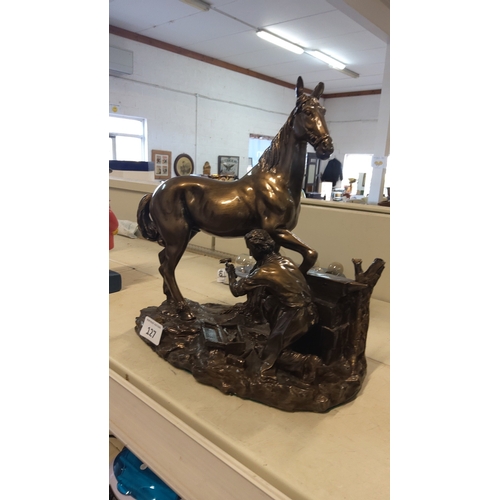 127 - Bronze-toned group of a standing horse with raised foreleg, accompanied by a kneeling farrier at wor... 