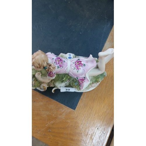 39 - Italian Capodimonte porcelain figure of a recumbent young girl holding flowers, wearing a pink dress... 