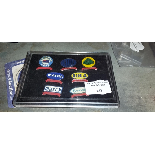 282 - 7 Motor Racing Enamel Pin Badges Including Bhabhan, Lola & Matra, In A Case