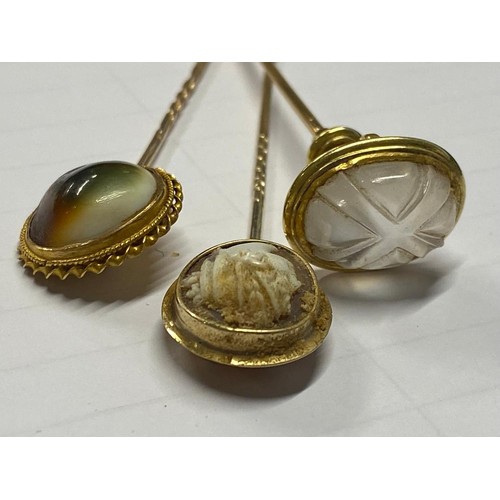 212 - Three yellow metal stick pins set with a cameo of a classical maiden, a carved rock crystal stamped ... 