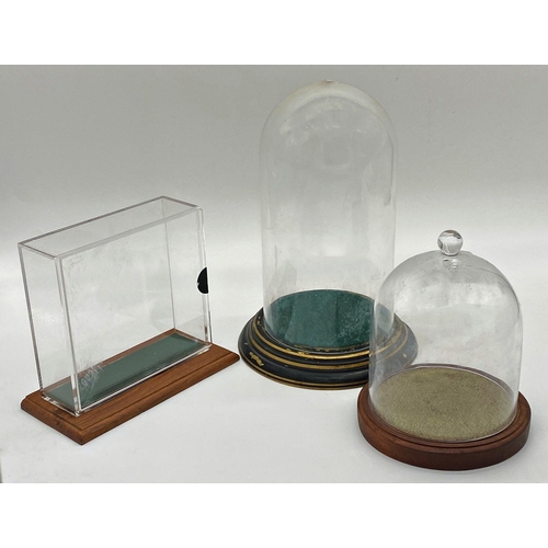 1104 - Two glass domes with bases, 29cm and 25cm high respectively with a further square Perspex example (3... 