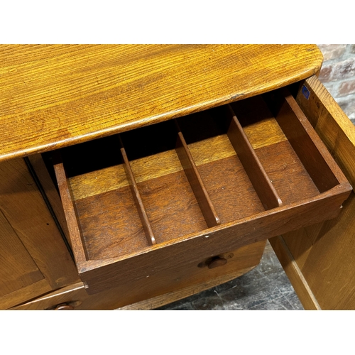 1202 - Ercol light elm sideboard, three cupboard doors over two drawers on casters, 76cm high x 130cm wide