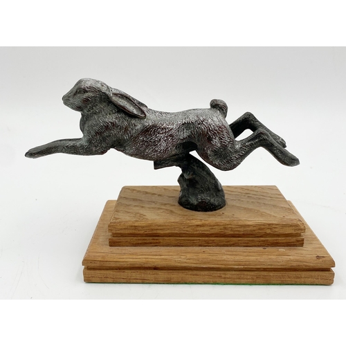 245 - Silvered bronze car mascot in the form of a leaping hare, on stepped oak plinth, 11cm high x 18cm lo... 