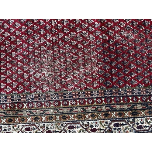 1454 - Large Persian wool full pile carpet with geometric paisley design upon a red ground, 340cm x 240cm.