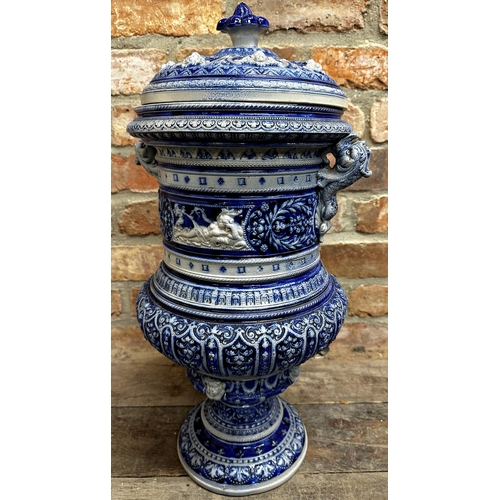 410 - Large Rhine ware pottery twin handled lidded pot, with panels of figures and foliage upon a blue gro... 