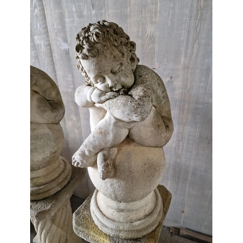 1041 - Pair of reconstituted stone cherub figures seated upon sphere cap finials, raised on column pedestal... 