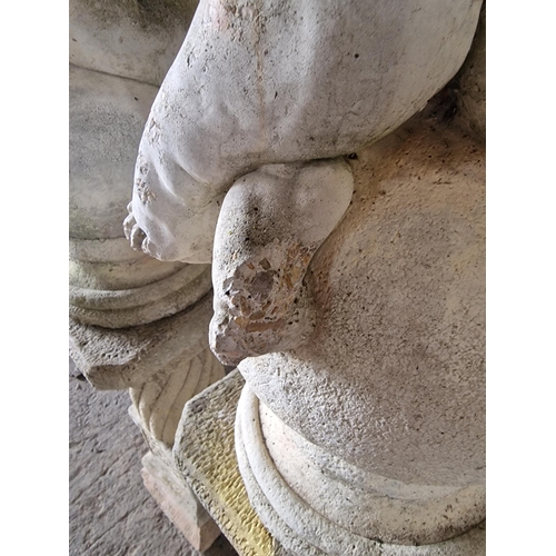 1041 - Pair of reconstituted stone cherub figures seated upon sphere cap finials, raised on column pedestal... 