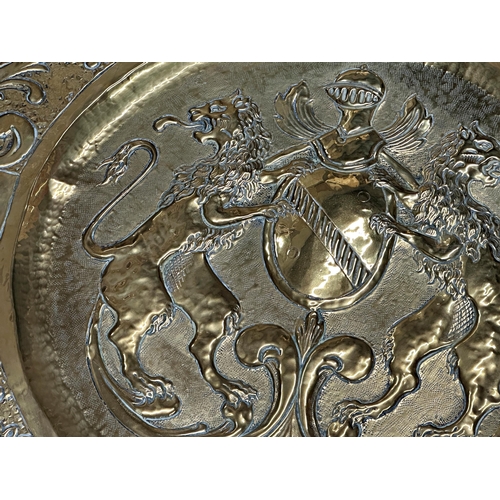 2400 - Large Arts and Crafts brass charger, embossed with coat of arms and scrolled acanthus boarders, 69cm... 