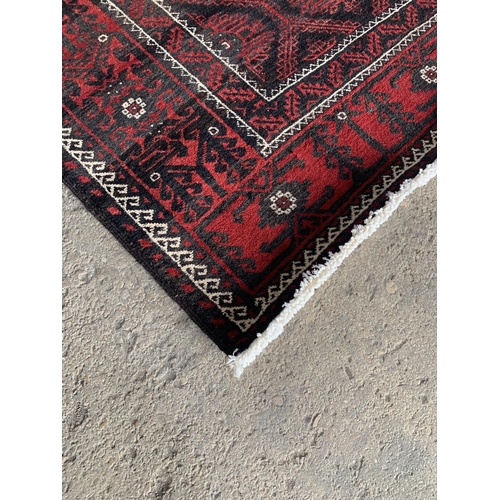 1430 - Persian Meshad Belouch rug with geometric red decoration on black ground, 220 x 115cm