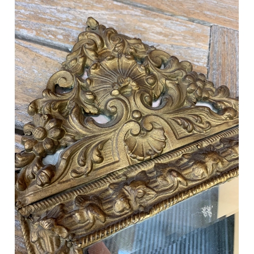 2415 - Antique repousse gilt cushioned mirror having original bevelled glass with floral and scalloped surr... 